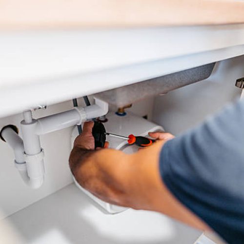 Mid-adult plumber fixing plumbing under the kitchen sink in an apartment. Close-up.